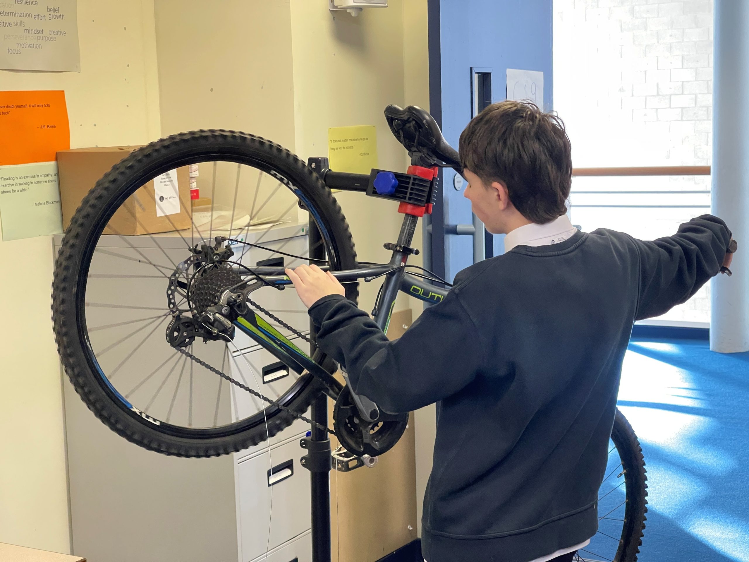 A boy is pictured from the back as he works on a bike, which is on a stand.