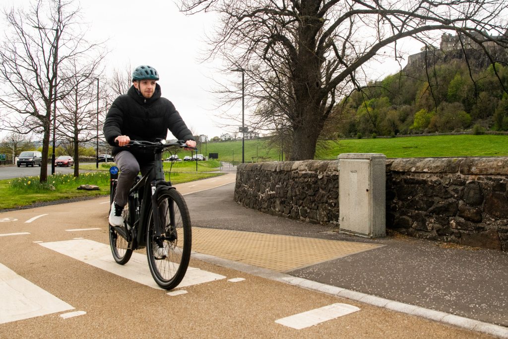 a man in black clothes and a helmet cycles along an orange path, part of Stirling's new cycle pathways