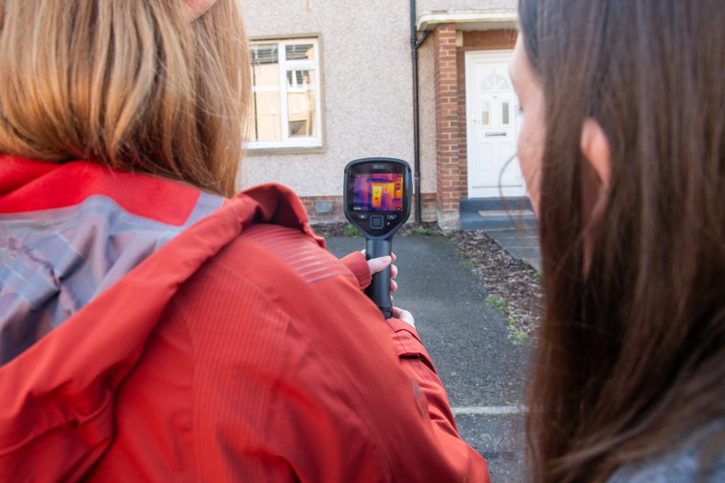 A FEL employee holds a thermal imaging camera, pointed at the front door of a house. It shows where heat is escaping.