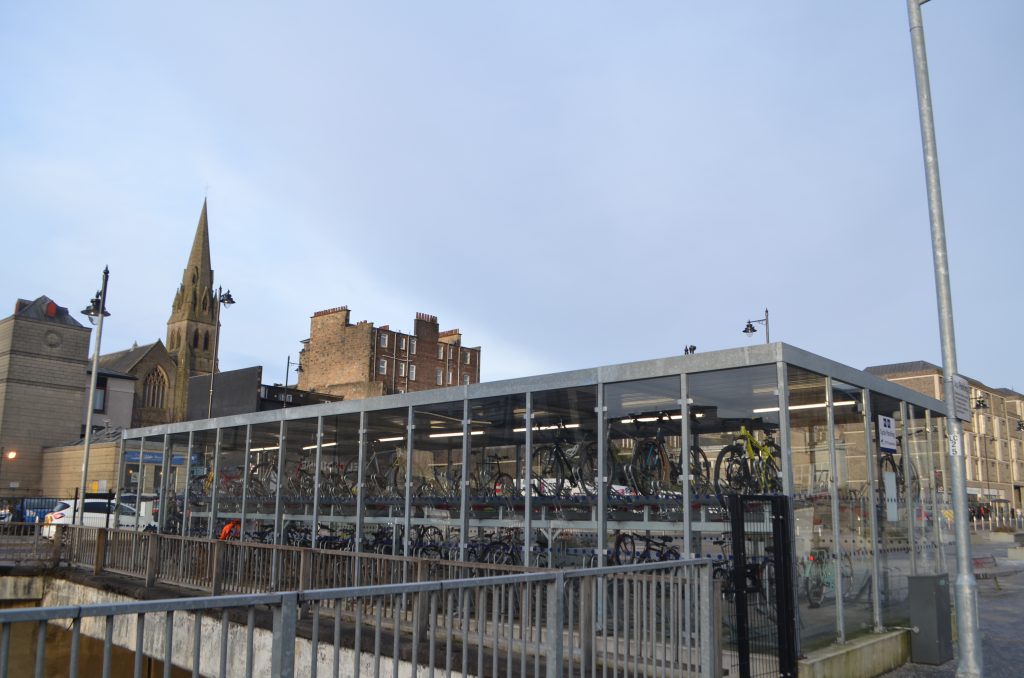 A photo of the well-used glass bike storage shed outside of Stirling train station, on a clear day