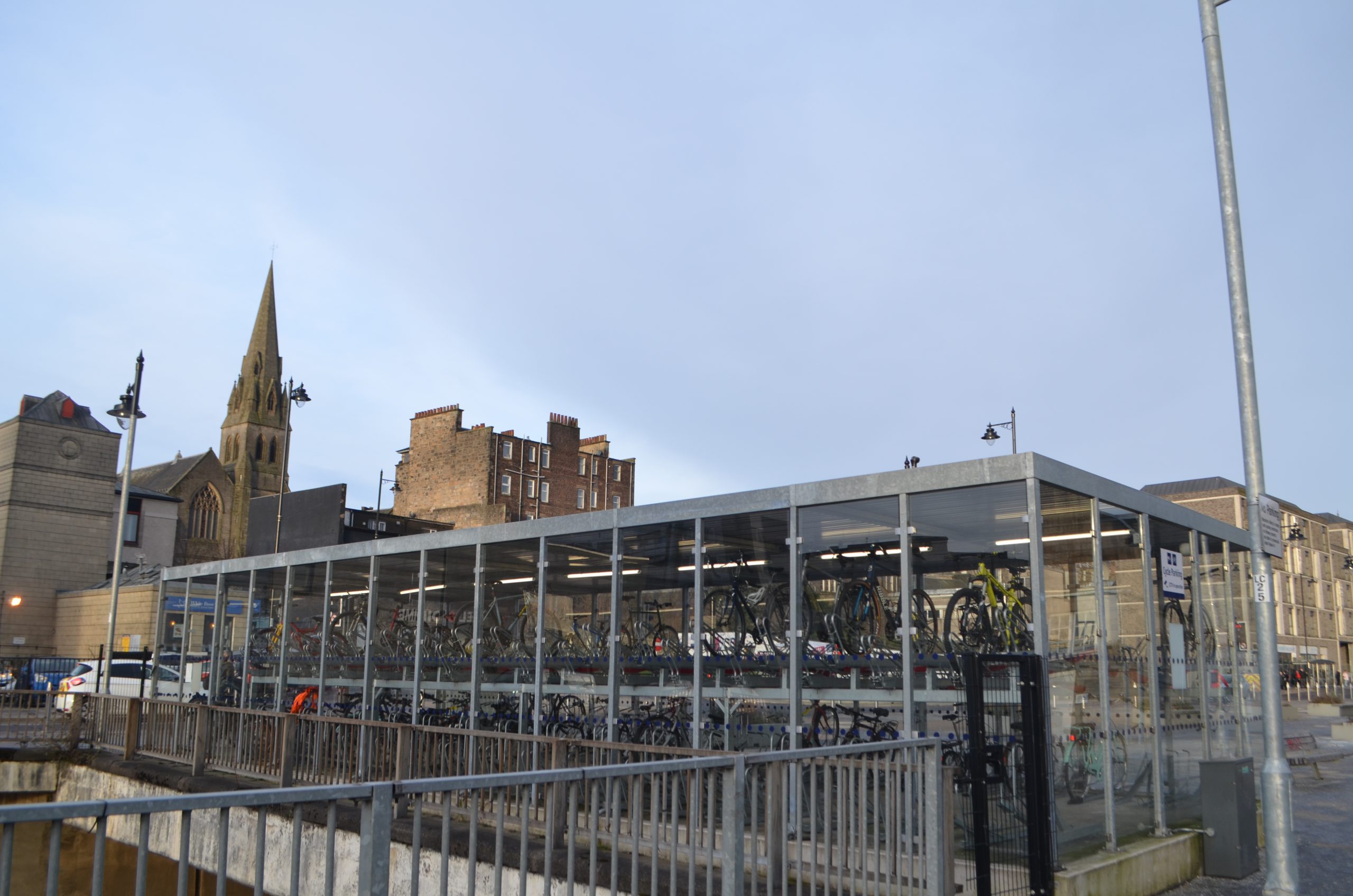 A photo of the well-used glass bike storage shed outside of Stirling train station, on a clear day