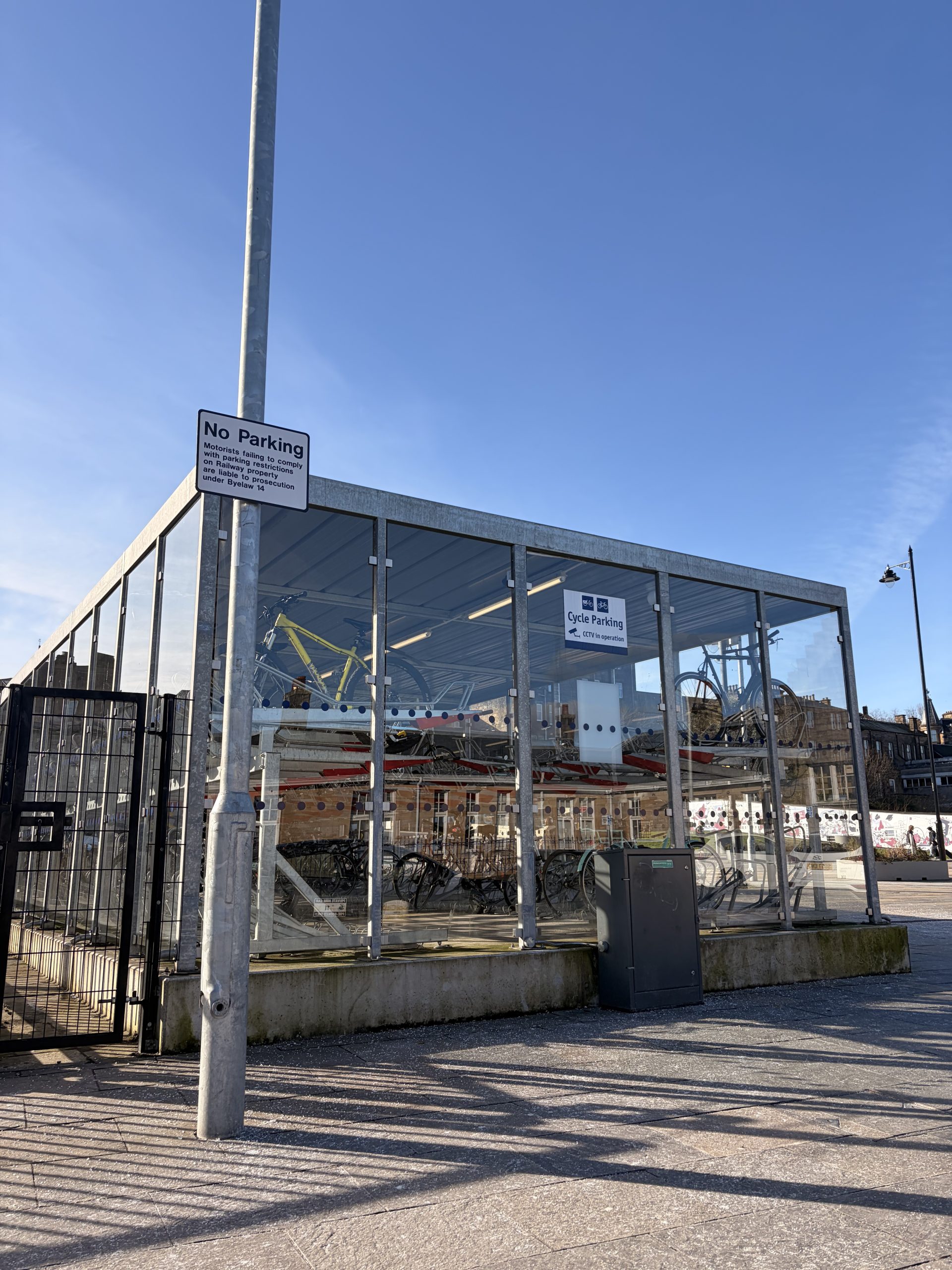 A photo of a full and well-used bike storage shed outside of Stirling train station, on a sunny day.