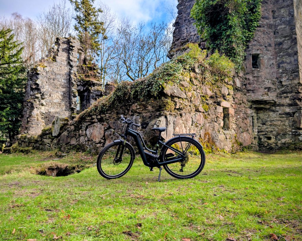 A black e-bike in the grounds of a castle on a sunny day